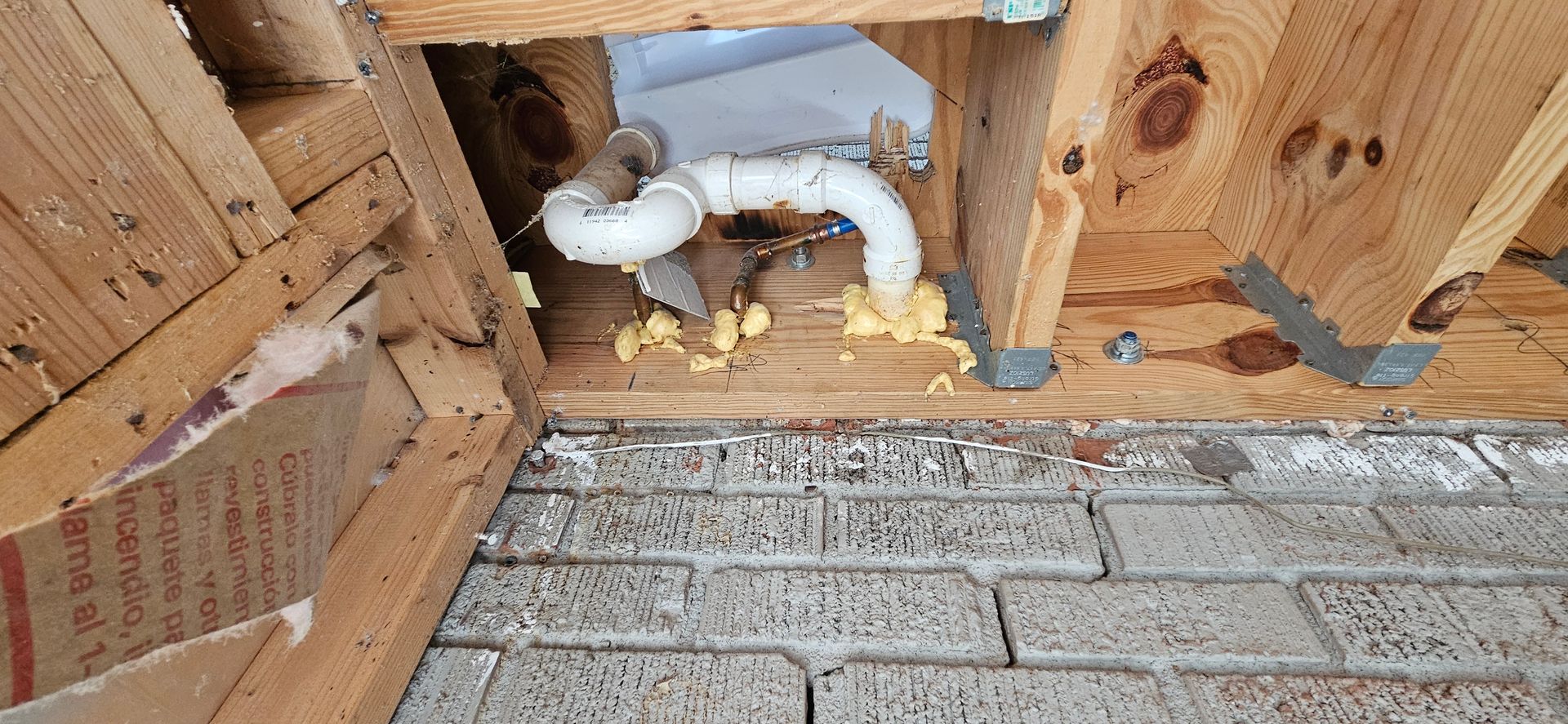 Plumbing pipes in a wooden structure, surrounded by foam and bricks.