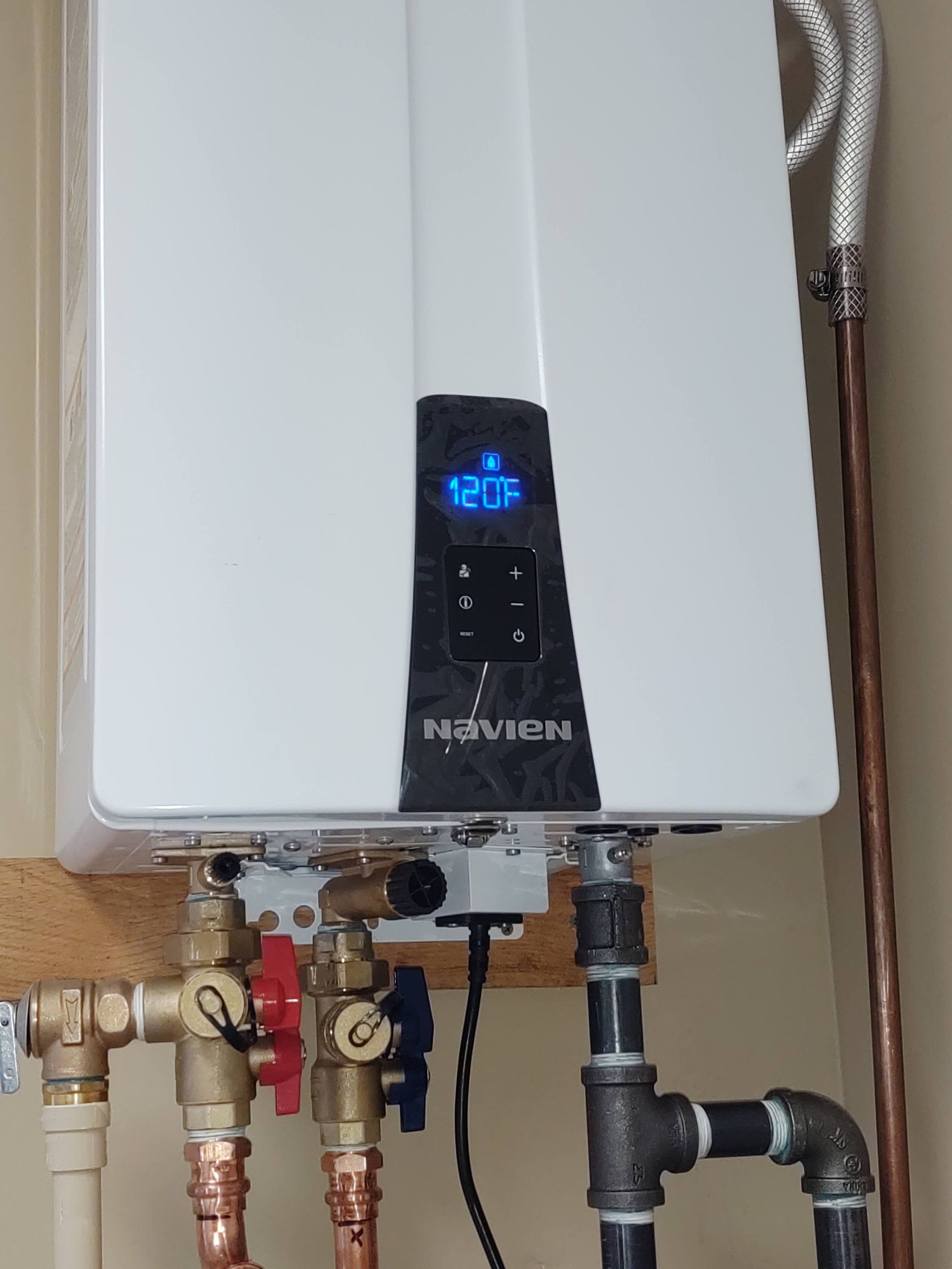 White Navien tankless water heater mounted on a wall with copper and black pipes connected.