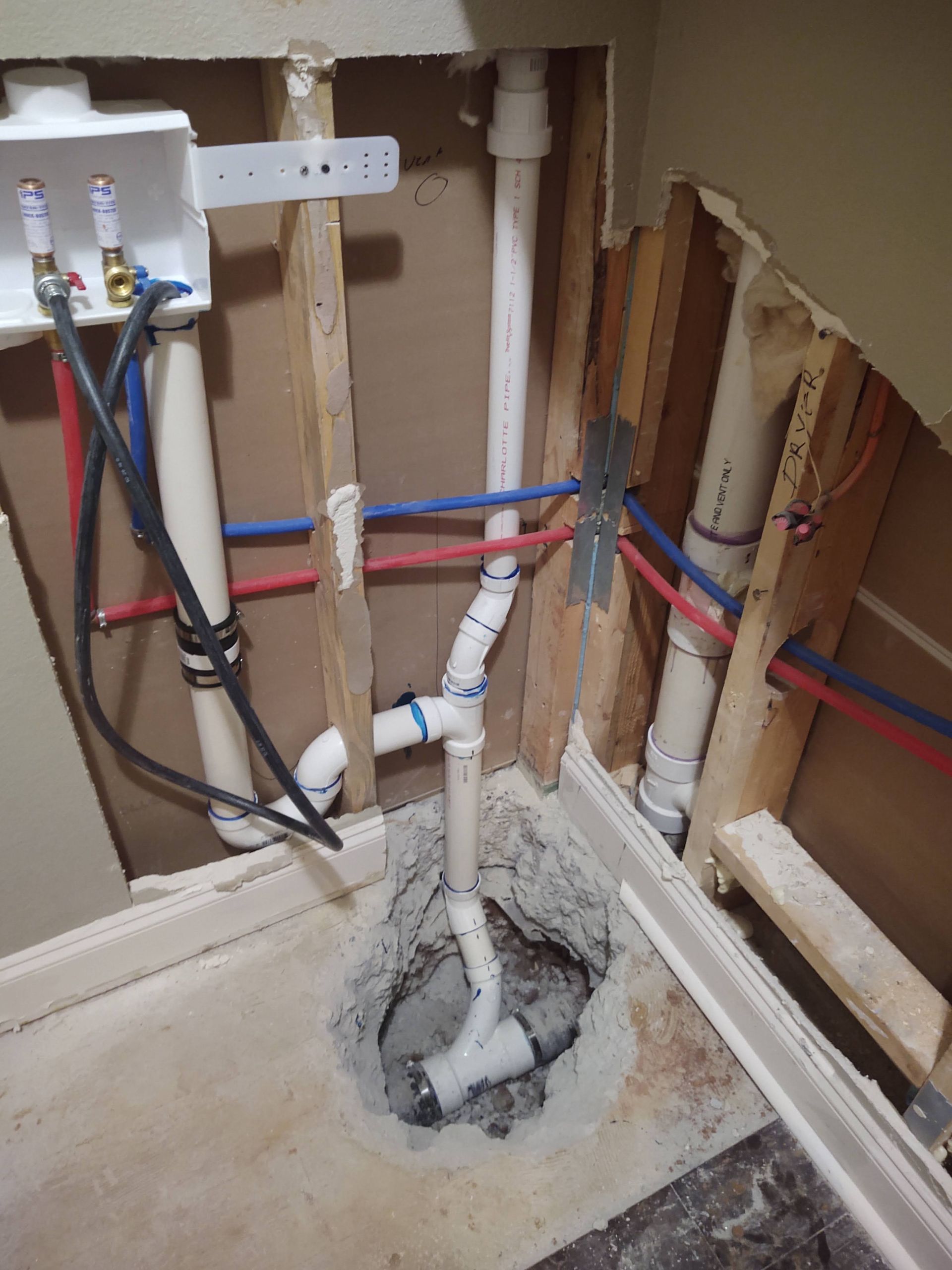 Plumbing rough-in within wall; pipes, wires, and a drain in concrete floor.