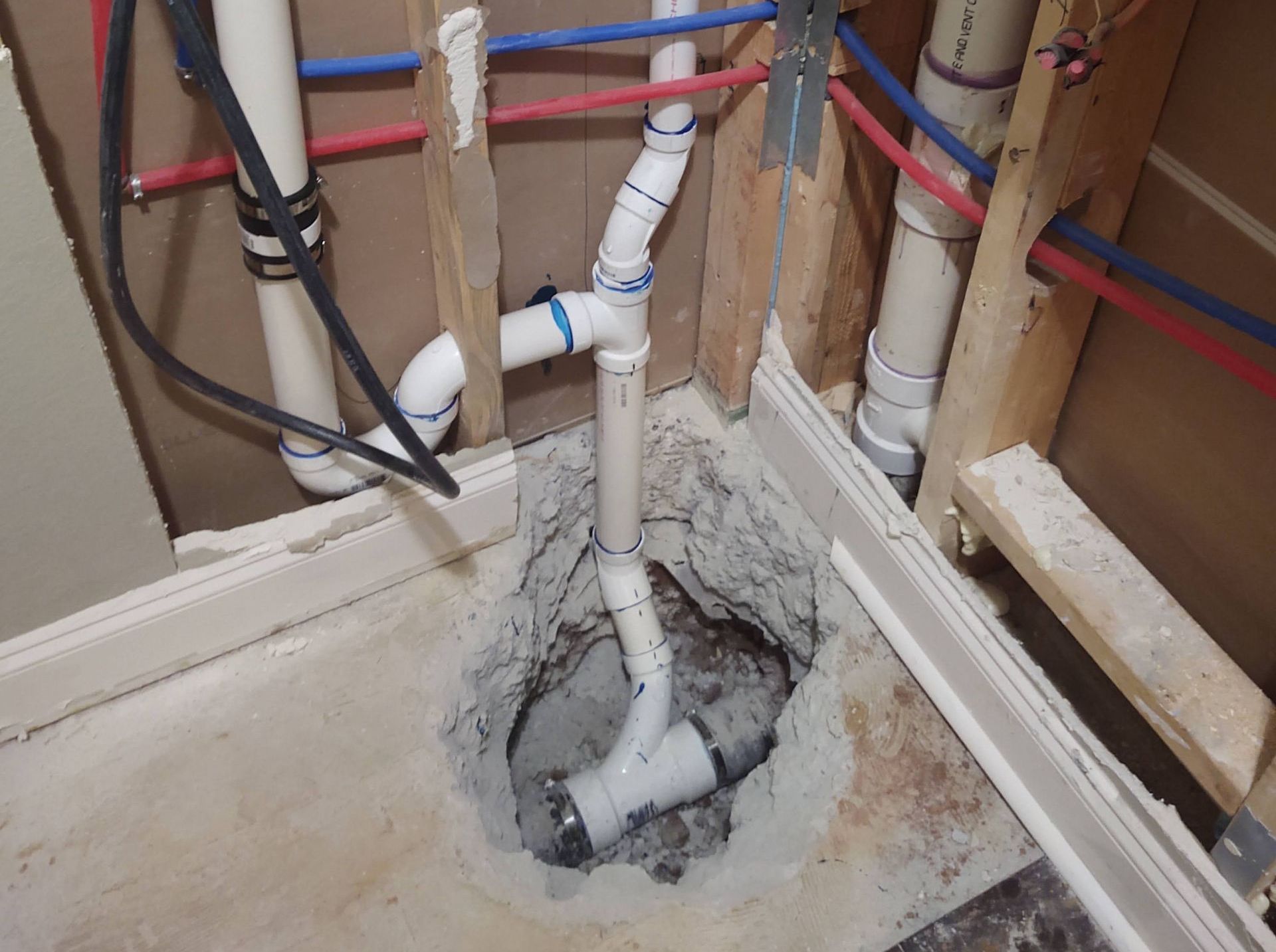 Plumbing pipes in a wall opening; white PVC pipes and blue/red water lines, exposed studs.