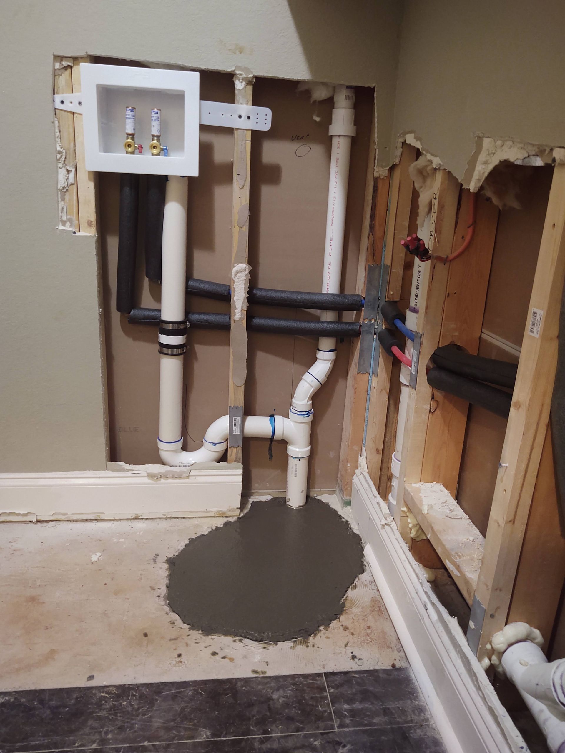Laundry room plumbing under construction, showing pipes, a water box, and concrete on the floor.