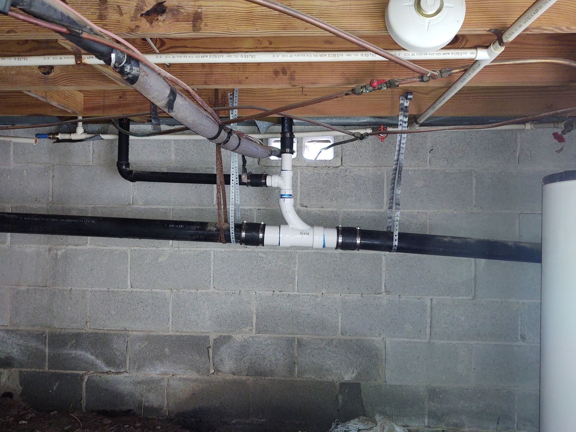 Black and white plumbing pipes against a gray cinder block wall in a basement.