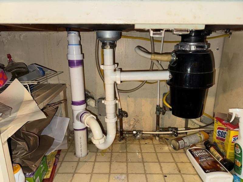 Under-sink plumbing: disposal, pipes, and p-trap beneath a white countertop.