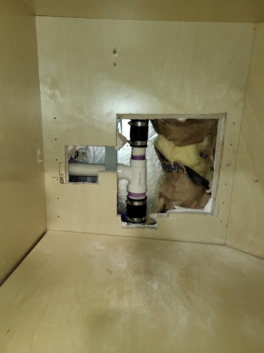 Plumbing pipes exposed within a wooden cabinet, with insulation visible.