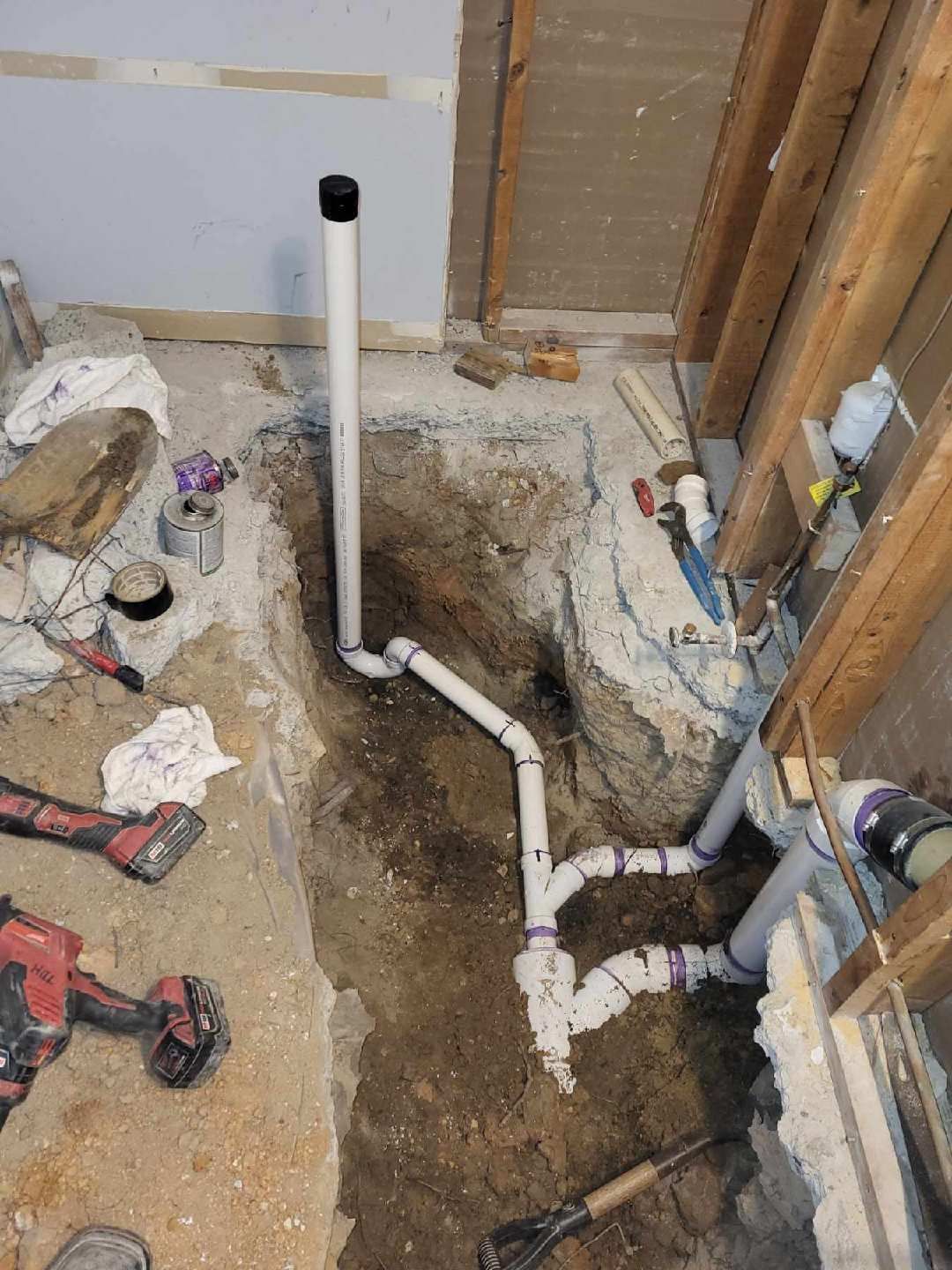 Plumbing pipes in a trench, with a vent pipe rising up. Construction site, dirt, and tools.