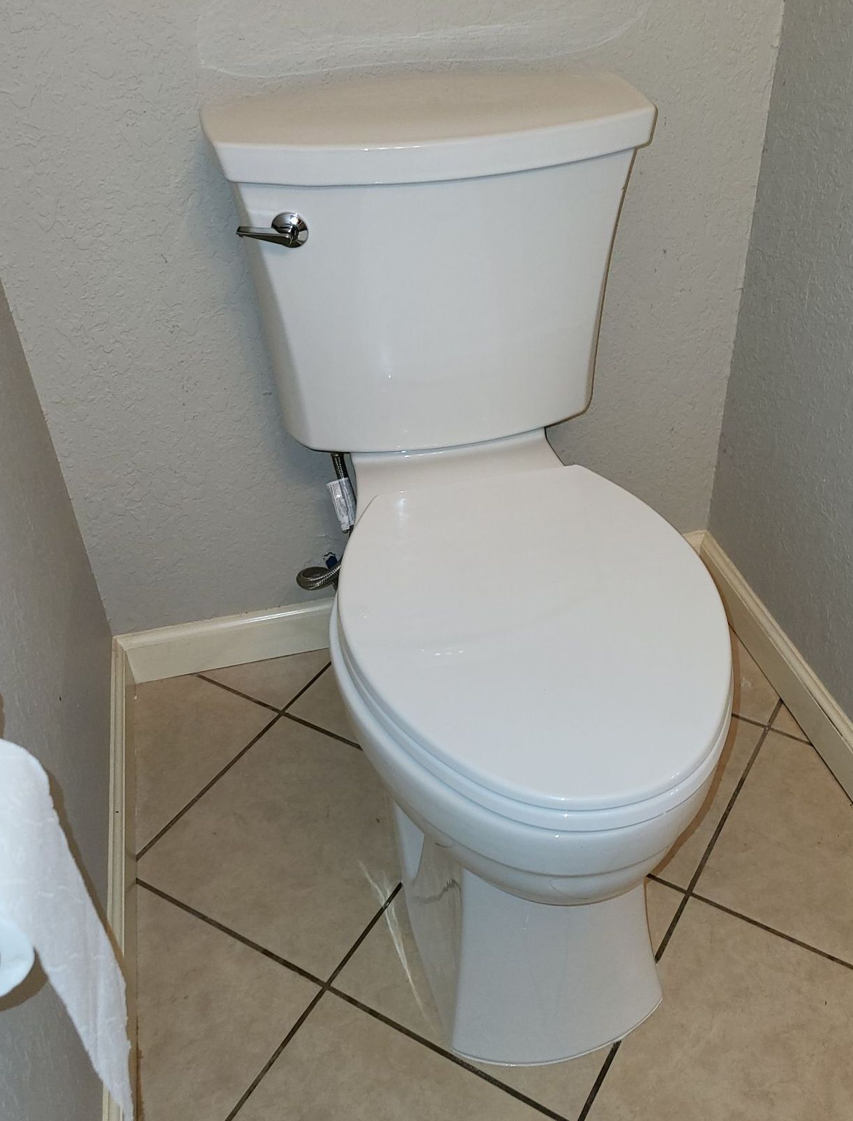 White toilet in a small bathroom, next to a gray wall, with beige tile floor.