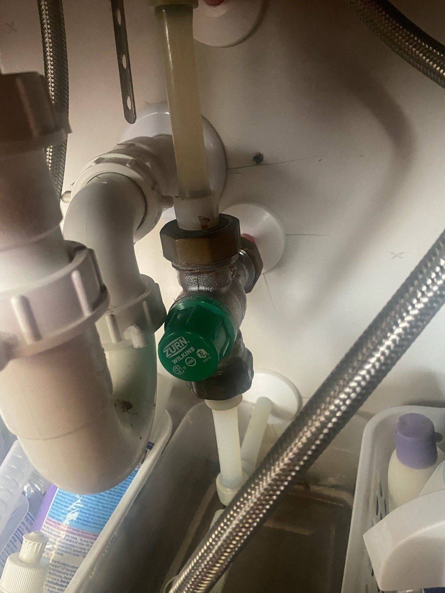 Green valve under a sink connected to pipes and a braided hose.