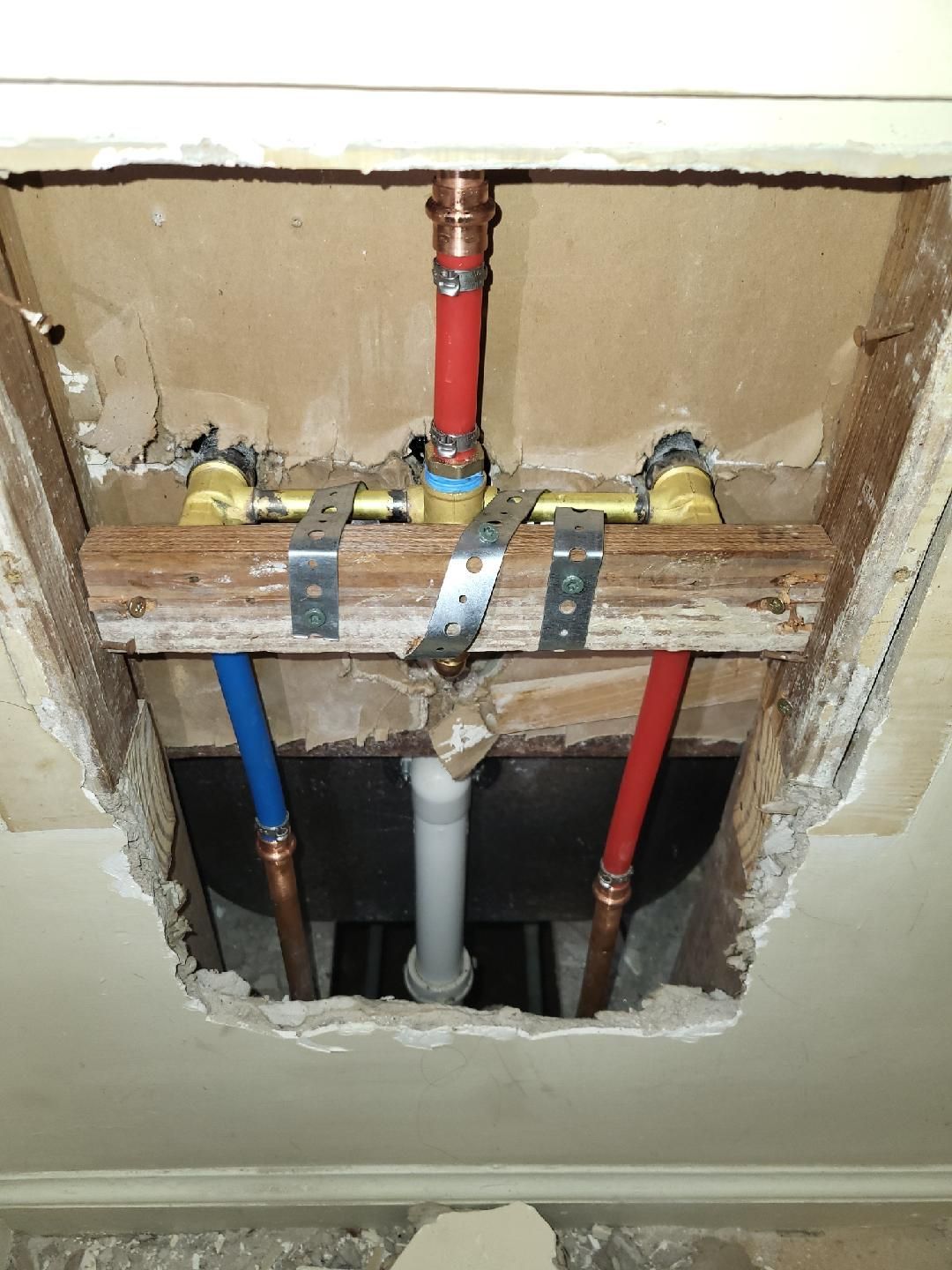 Plumbing pipes with copper and PEX connected above a bathtub. Red, blue, and white pipes are visible within a ceiling cavity.