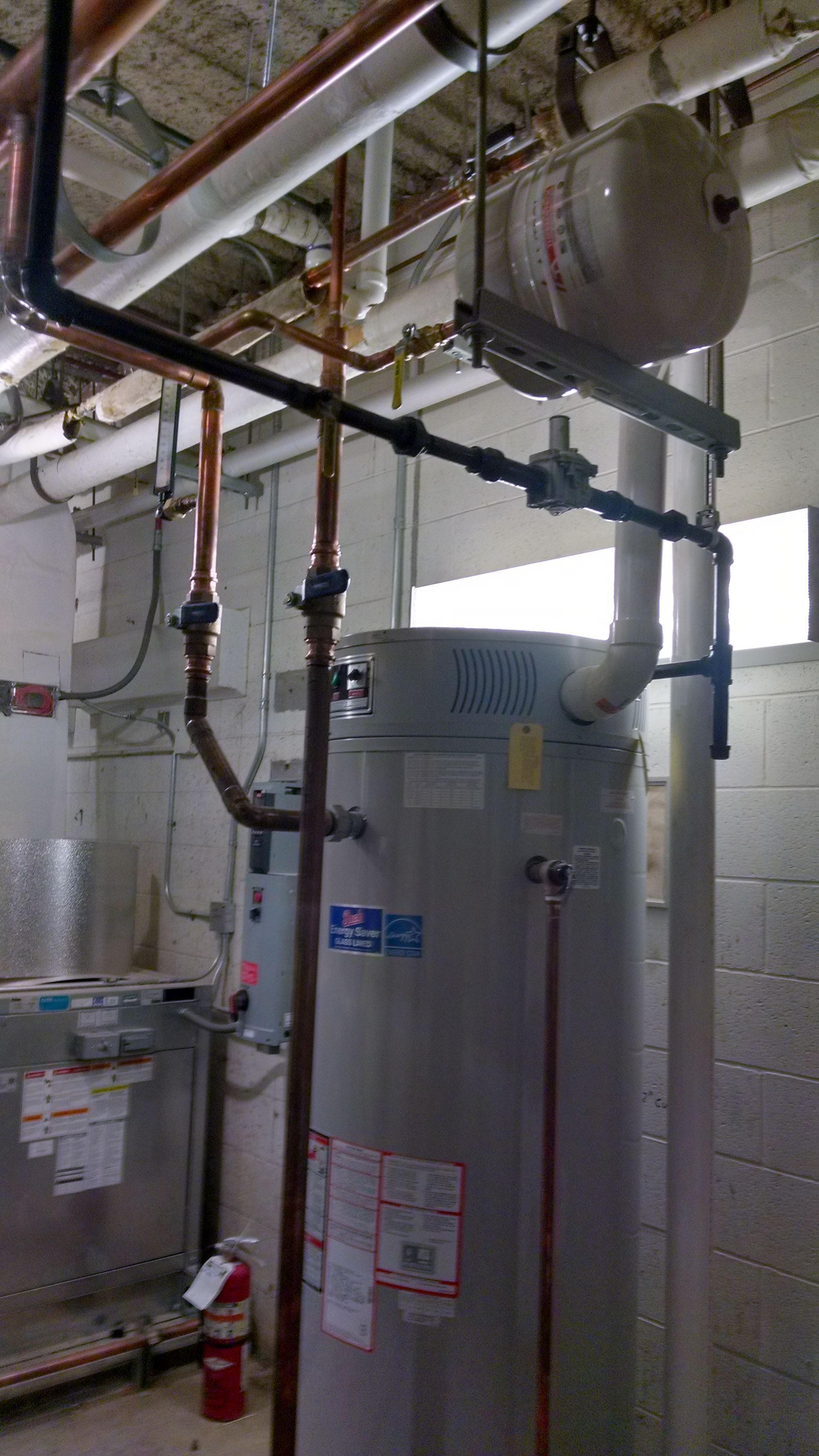 Water heater and pipes in a utility room with a fire extinguisher nearby.