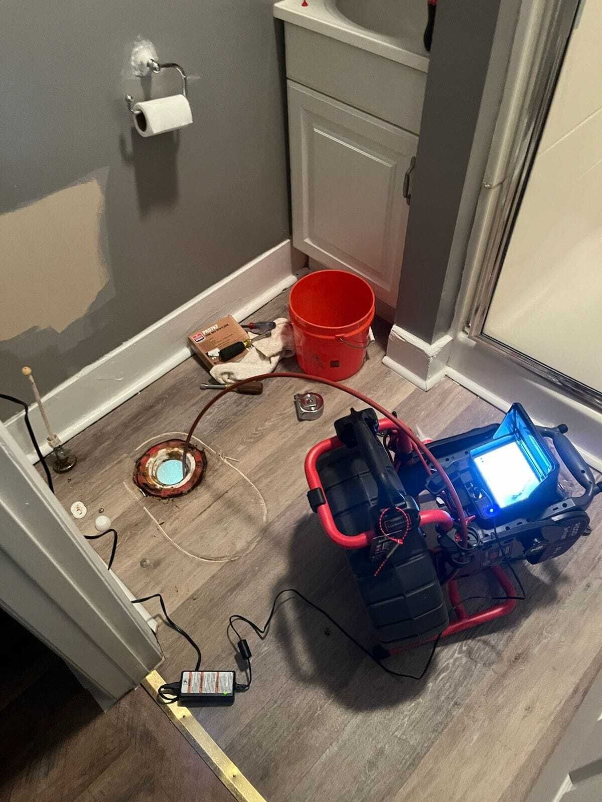 Bathroom with plumbing inspection equipment. A red cart with a screen, copper coil, and bucket on floor.