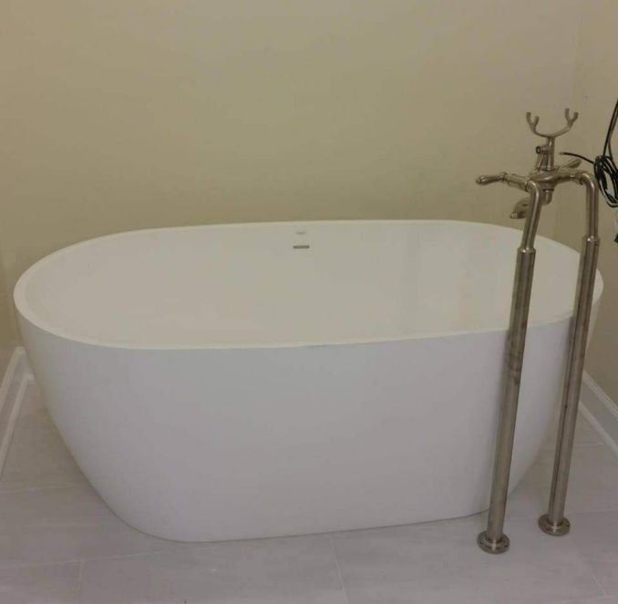 White oval freestanding bathtub with silver faucet fixtures.