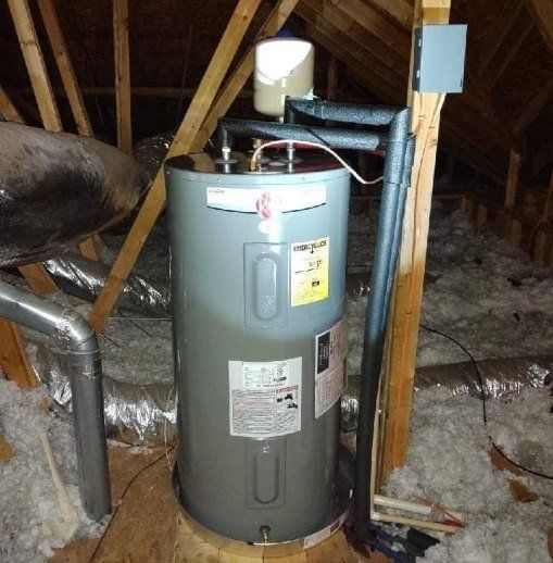 Water heater in attic, surrounded by insulation, vent pipes, and wooden beams.