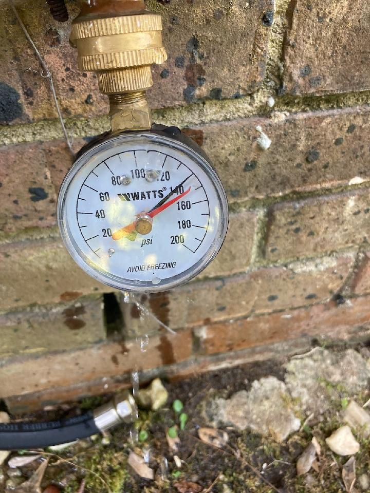 Water pressure gauge mounted on a brick wall reads approximately 80 PSI. A hose is connected.