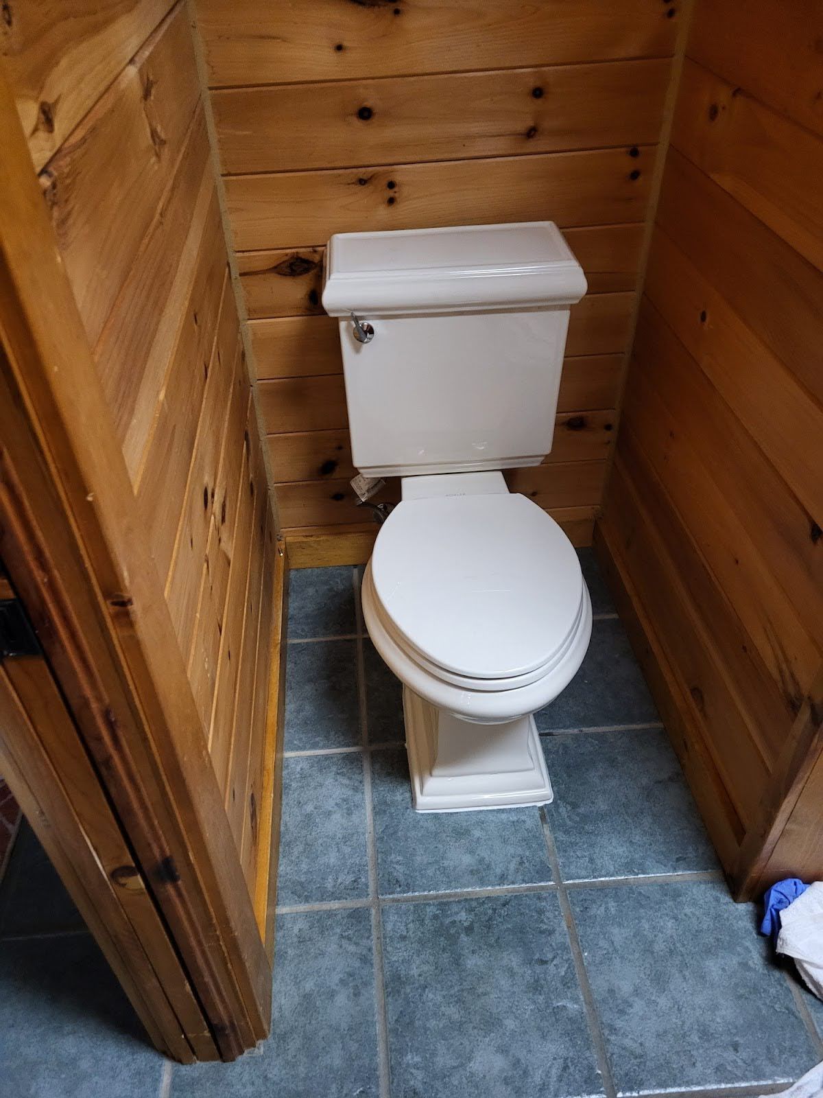Toilet in a small, wood-paneled bathroom with blue tile flooring.