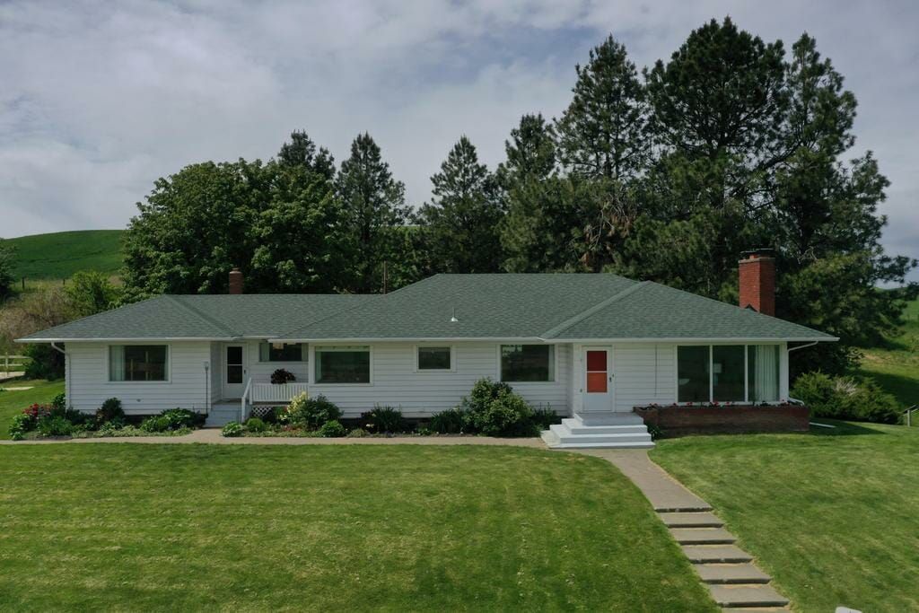 A white house with a green roof is surrounded by trees