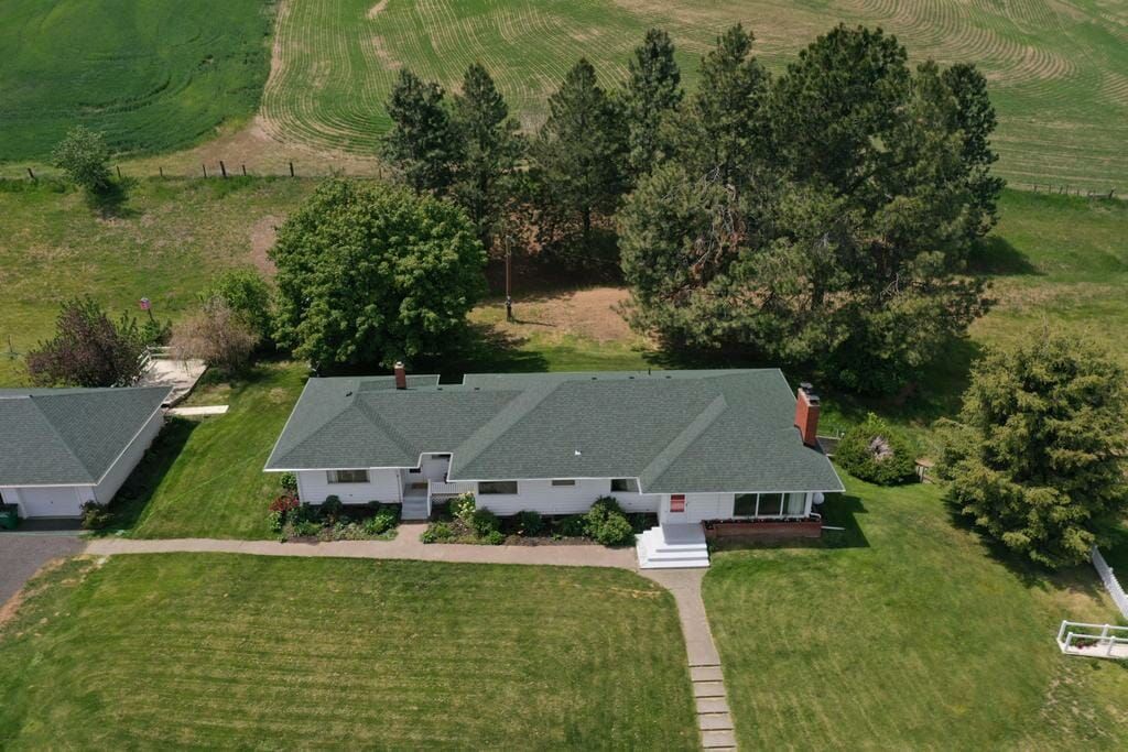 An aerial view of a house in the middle of a grassy field surrounded by trees.