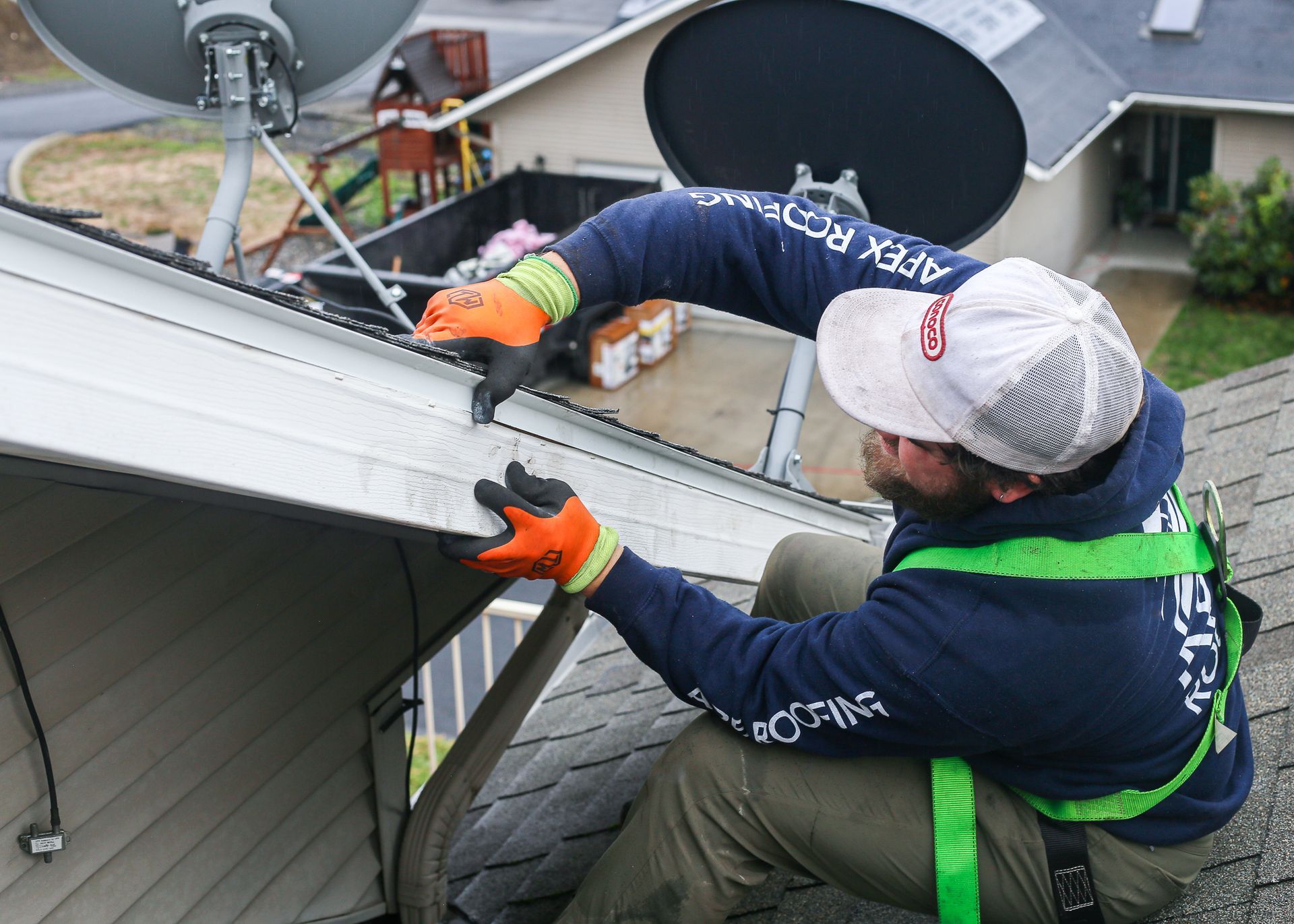 A man is working on a roof with a satellite dish in the background.