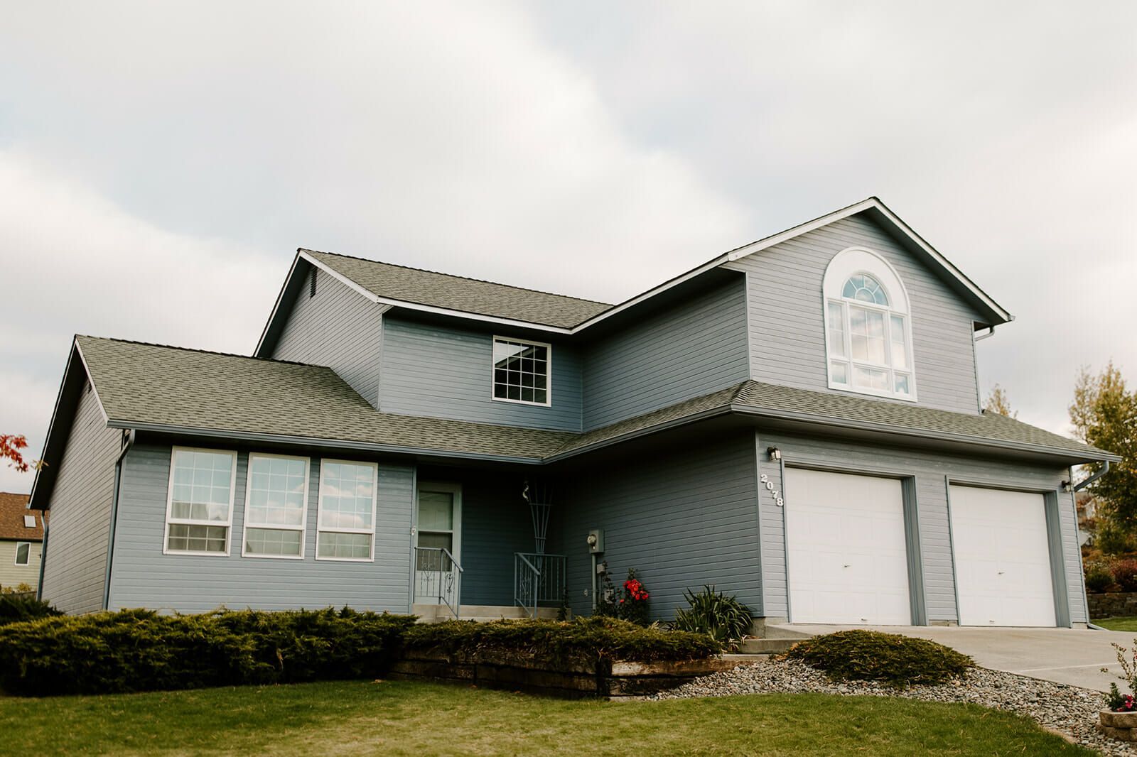 A large blue house with a green roof and white garage doors.