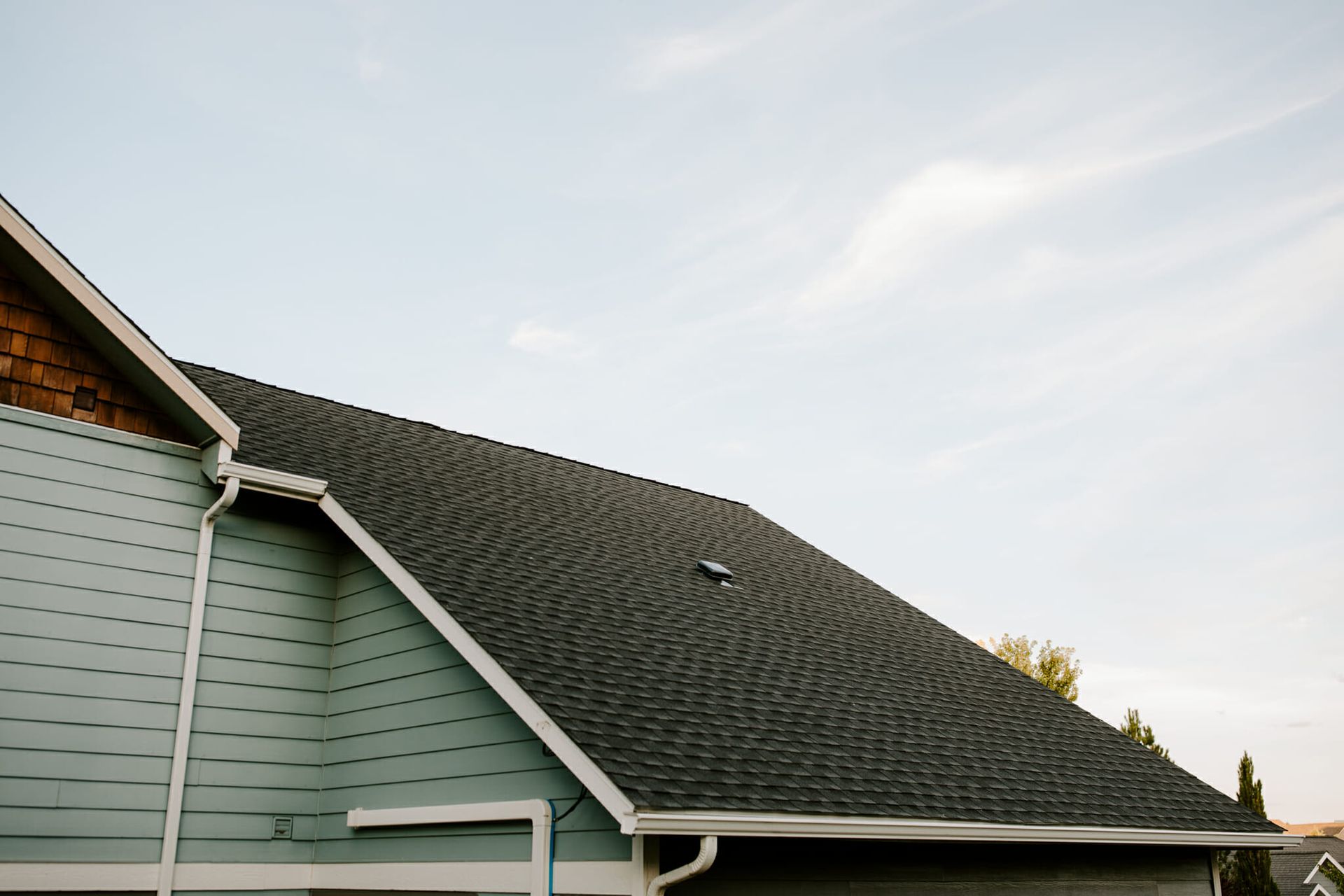 A house with a black roof and a blue siding is against a blue sky.