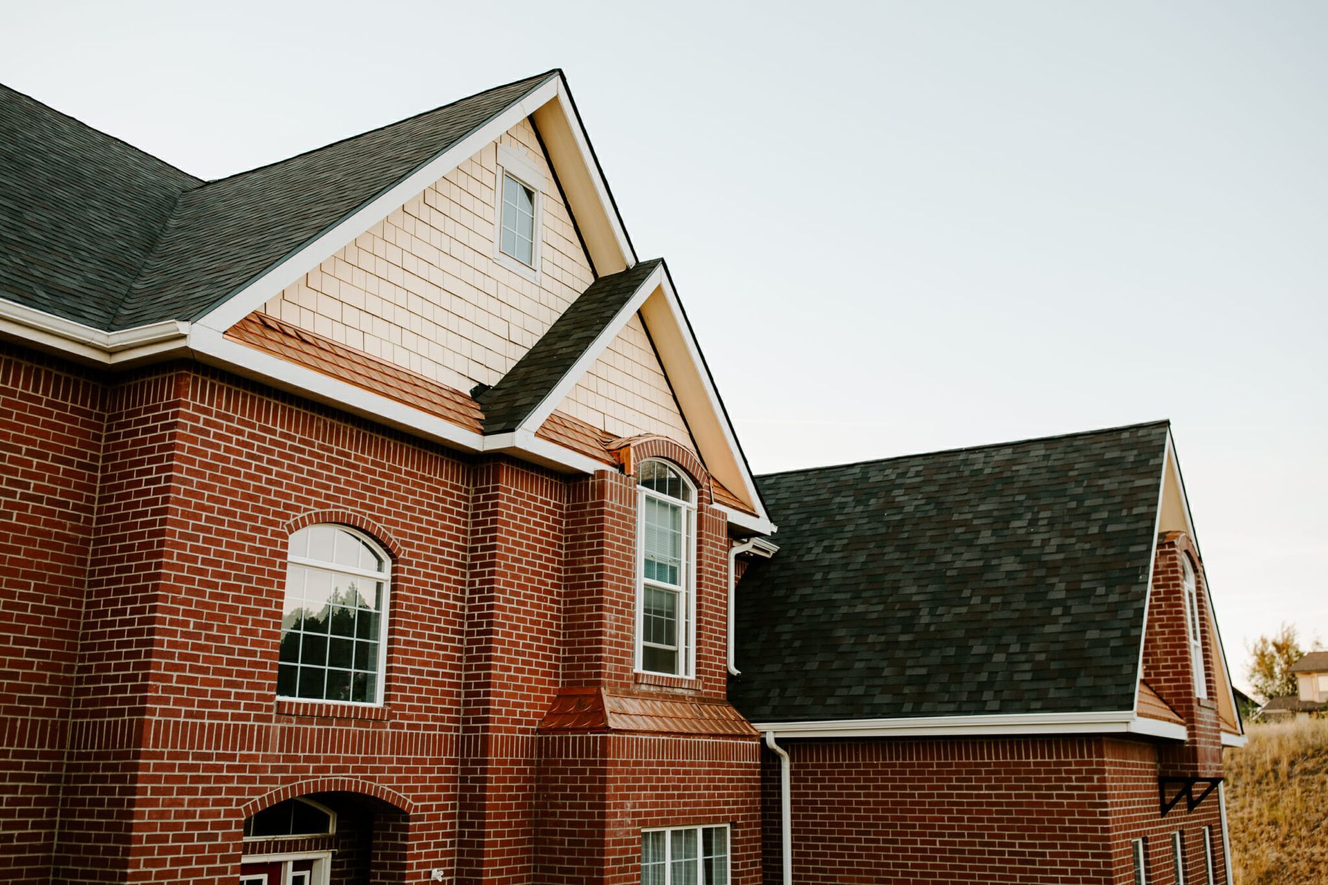A large brick house with a black roof and white siding.