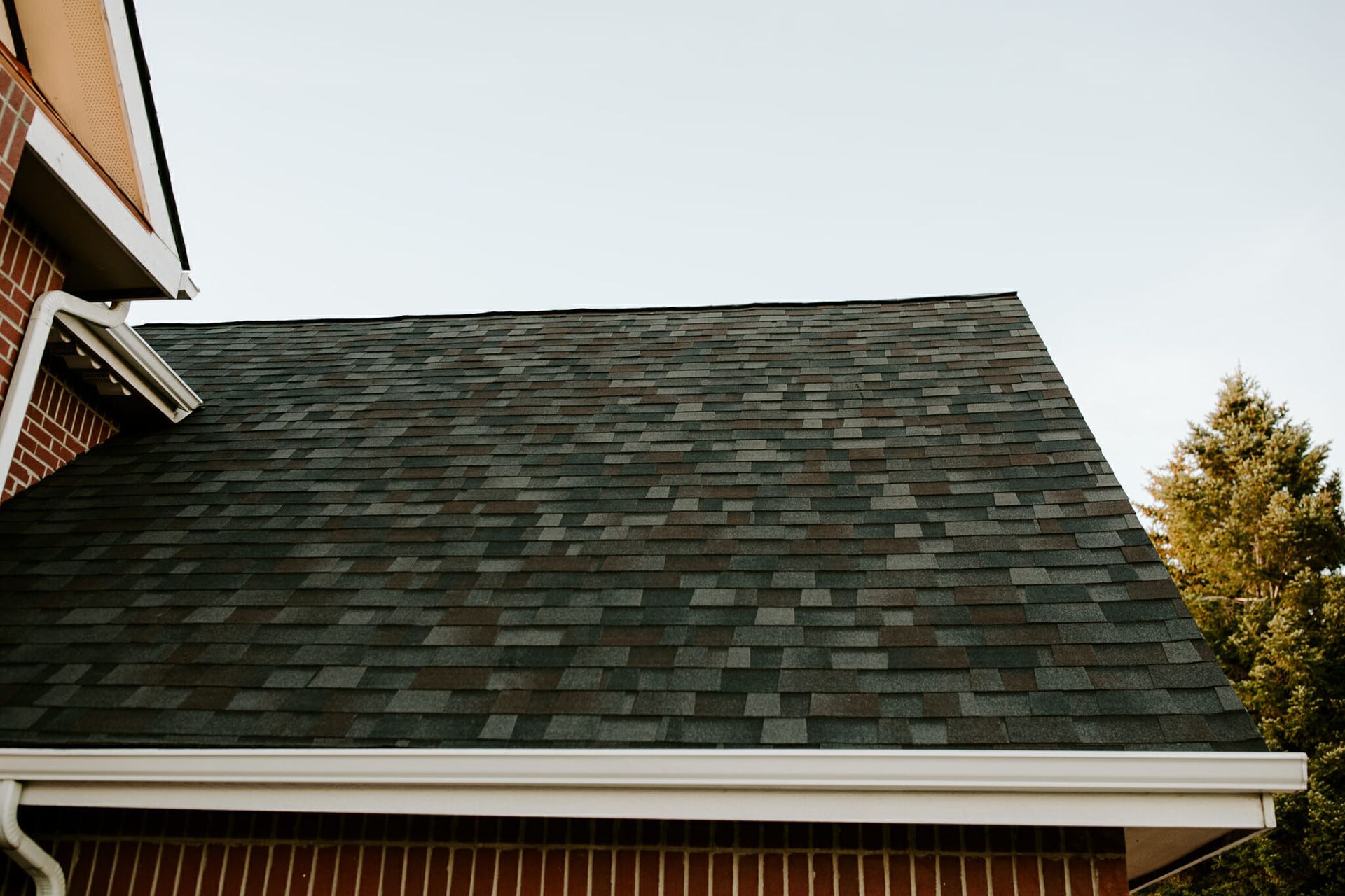 A brick house with a black roof and a white gutter.