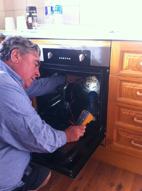 Man in Blue Shirt Checking Oven Temperature With a Yellow Device in a Kitchen — Abode Electrical in Tighes Hill, NSW