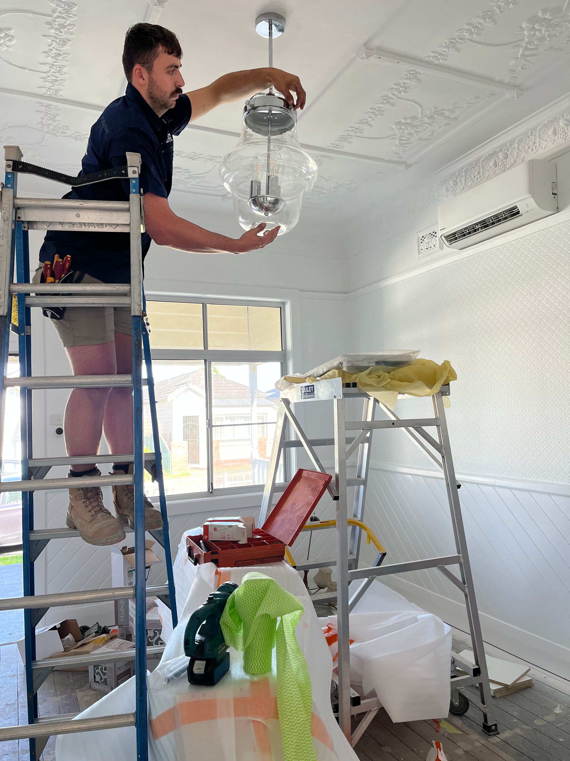 Electrician installing a light fixture on a patterned ceiling — Abode Electrical in Tighes Hill, NSW