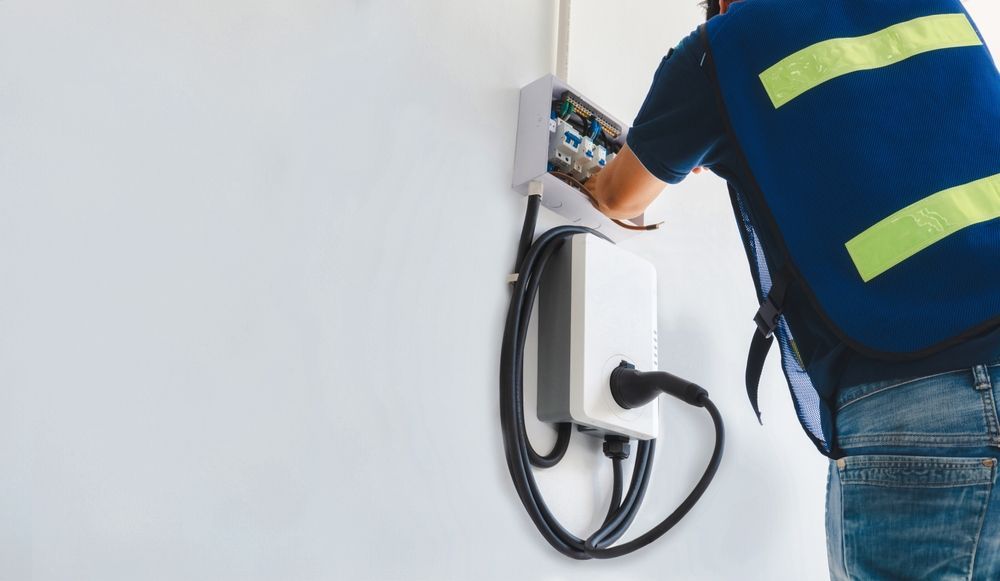 Electrician Installing an Ev Charger on a White Wall — Abode Electrical in Tighes Hill, NSW