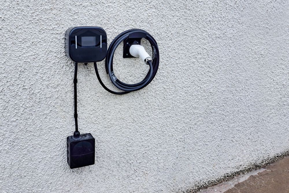 Black EV Charger Mounted on a Textured White Wall, With Cable and Plug Visible — Abode Electrical in Mayfield, NSW
