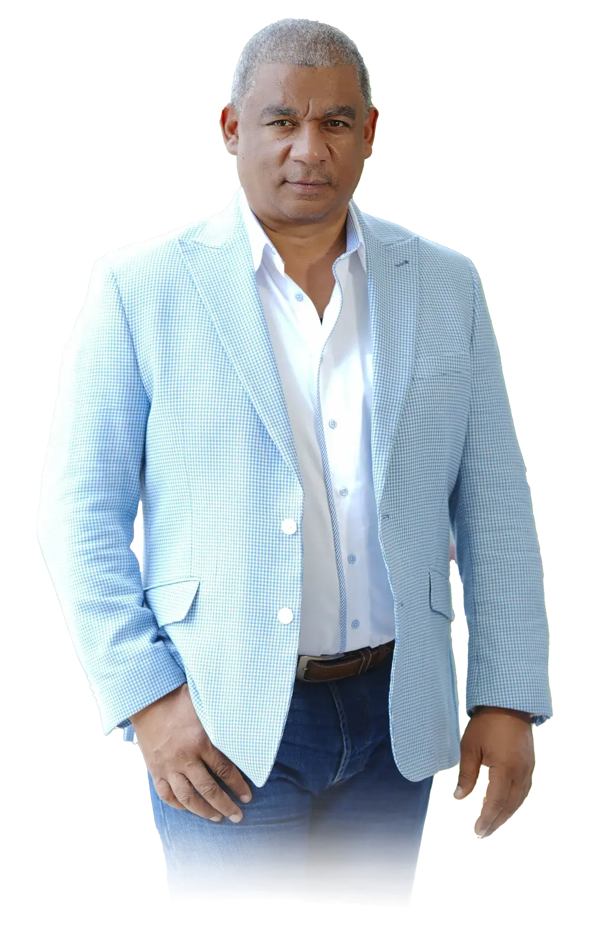 Man in a blue blazer and jeans stands facing the camera. He has dark skin and gray hair, with one hand in his pocket.