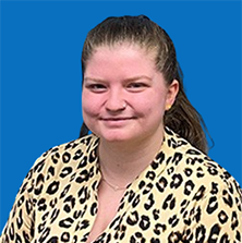 Woman with brown hair, nose ring, smiling at the camera, against a blue background.