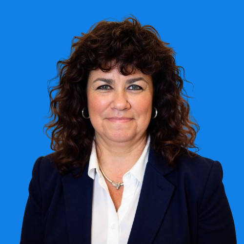 Woman with curly brown hair and pearl necklace smiles. Blue background.