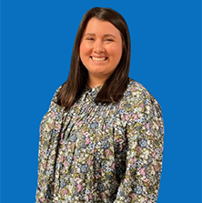 Woman with brown hair, smiling, wearing a floral shirt, against a blue background.