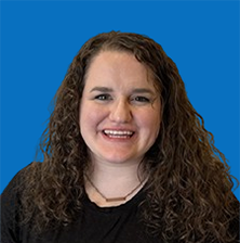 Woman with brown hair smiling, wearing pearl earrings, against a blue background.