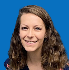 Woman with long brown hair smiling in front of a blue background.