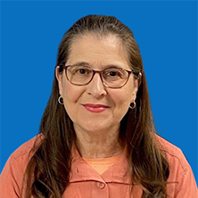 Woman with glasses and auburn hair smiling at the camera, wearing a coral-colored top, in front of a blue backdrop.