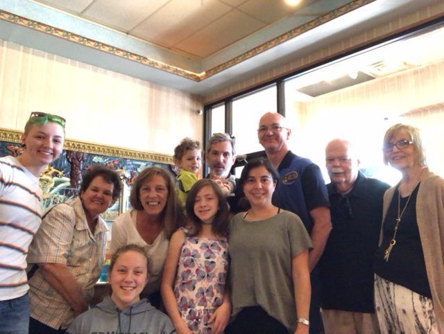 Group photo: Ten people smile at camera in a restaurant. Brightly lit with tall windows.