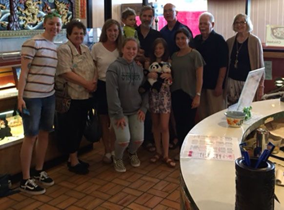 Group of people posing in front of a counter, likely a restaurant. Smiling faces, indoor setting, tiled floor.