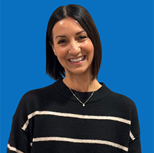 Woman with glasses smiles; burgundy shirt, against a blue wall.