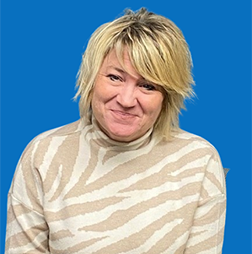 Blonde woman smiling, wearing a beige and white zebra-striped turtleneck, against a blue backdrop.