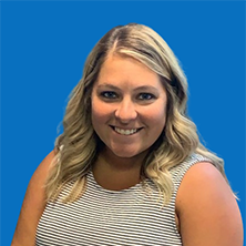 Blond woman with a warm smile, blue eyes, and wavy hair. Facing forward with a blue backdrop.