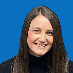 Woman with long brown hair smiling, wearing black, against a blue background.