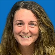 Woman with long brown hair smiling, blue eyes, against a light blue background.