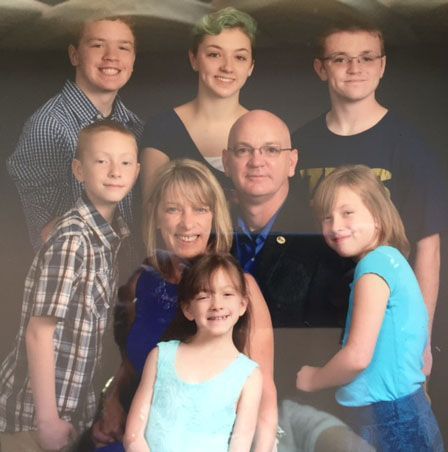 Family portrait: seven children and parents smiling against a gray backdrop.