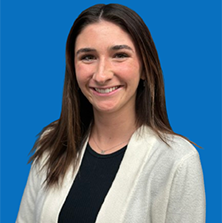 Woman with brown hair smiling, wearing a white cardigan and black shirt in front of a blue wall.