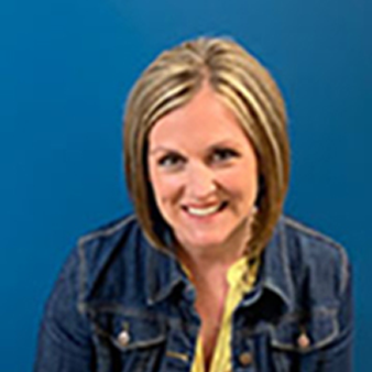 Woman with white hair, smiling, wearing a pink top with black trim, blue background.
