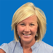 Blonde woman smiling, wearing striped blue top, dangling earrings, in front of a blue background.