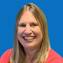 Blonde woman smiles broadly, wearing a coral top against a blue backdrop.