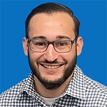 Man with glasses and a beard smiling, wearing a plaid shirt against a blue background.