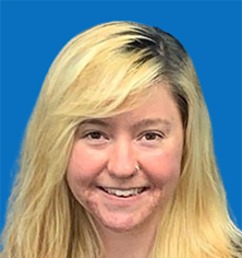 Blonde woman smiling, against blue background, wearing black cardigan over patterned blouse.